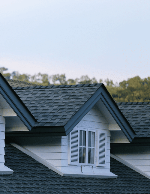 vaulted roof over small window with black and grey shingles and white siding