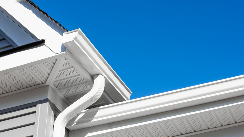 white gutters in the corner of a home with grey siding and clear blue sky in the background
