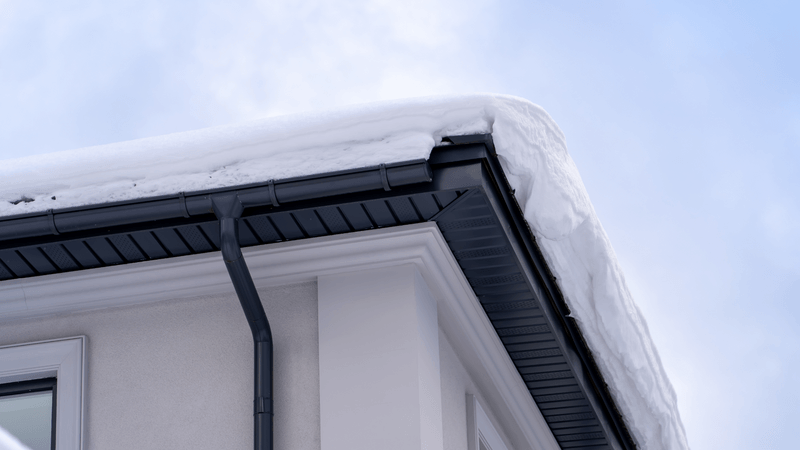 snow and ice built up on roof and black gutters of home