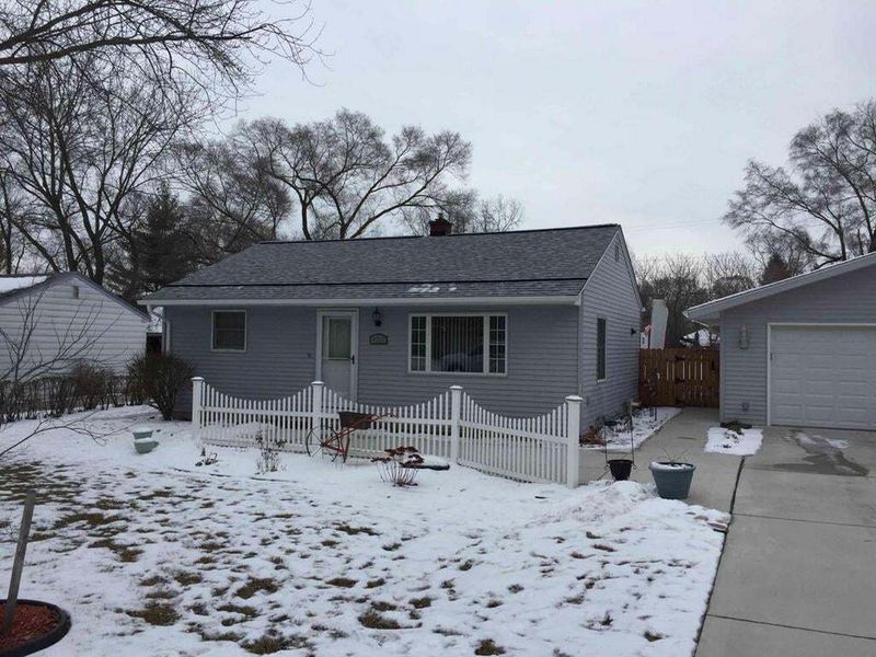 front of light grey home with snow on lawn white fence and black and grey roof shingles