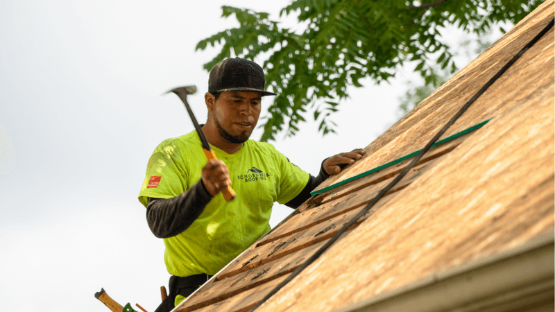 schoenherr roofing contractor standing on ladder hammering wood on roof