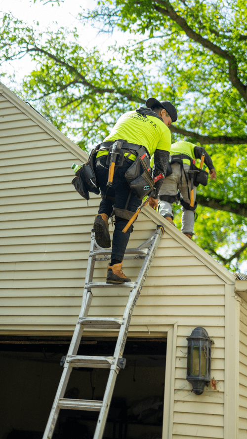 Schoenherr roofing specialists with toolbelts safely climbing on to roof of home using ladder